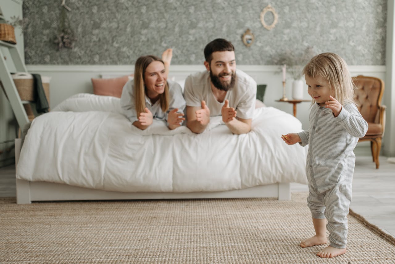 A joyful morning with parents encouraging their young child in a cozy bedroom setting.